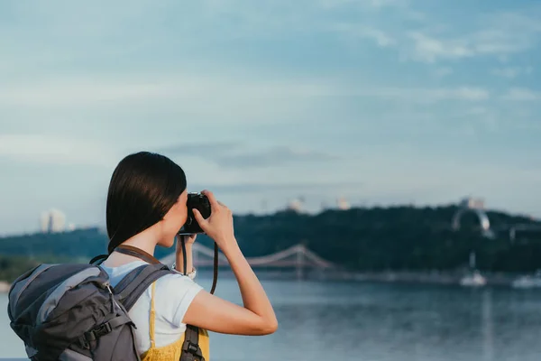 Back view of brunette woman with backpack taking photo — Stock Photo
