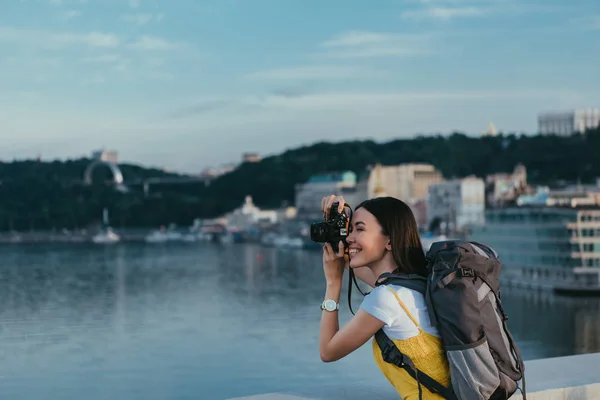 Vista lateral de mujer asiática con mochila tomando foto - foto de stock