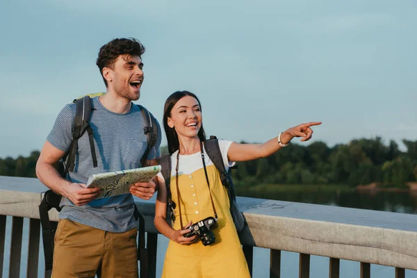 Guapo hombre sosteniendo mapa y asiático mujer apuntando con dedo - foto de stock