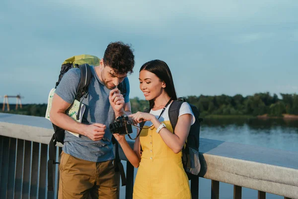 Bel homme et asiatique femme en salopette regardant appareil photo numérique — Photo de stock