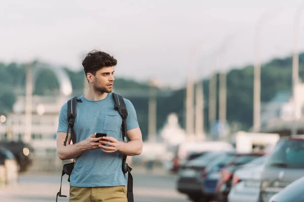 Bel homme en t-shirt tenant smartphone et détournant les yeux — Photo de stock