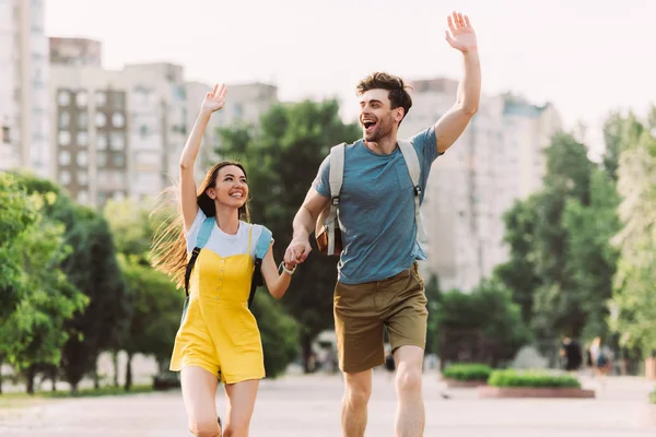 Handsome man and asian woman running and waving outside — Stock Photo