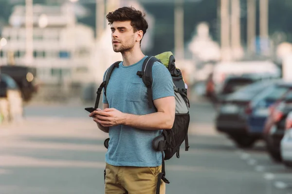 Handsome man in t-shirt holding smartphone and looking away — Stock Photo