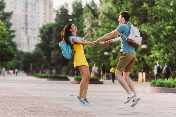 Homme et asiatique femme sourire, sautant et tenant la main — Photo de stock