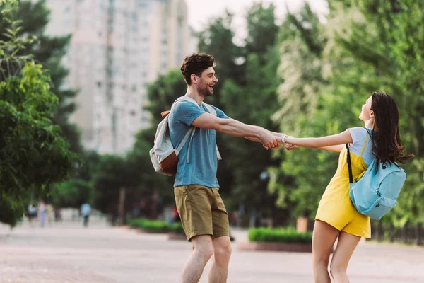 Handsome man and woman with backpacks smiling and holding hands — Stock Photo