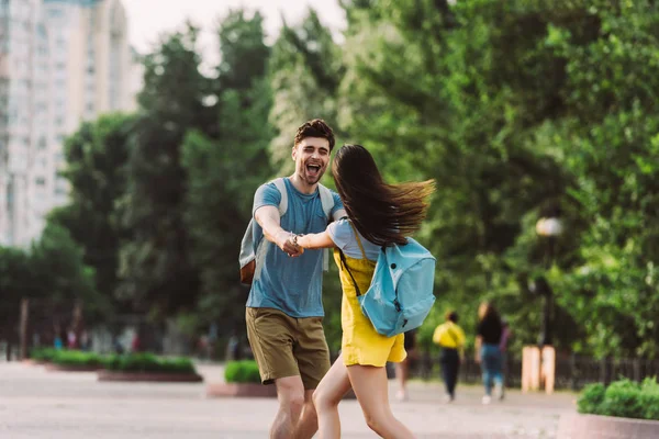 Красивый мужчина и женщина с рюкзаками улыбаются и держатся за руки — стоковое фото