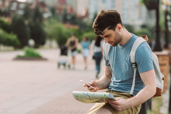 Handsome man in t-shirt using smartphone and holding map — Stock Photo