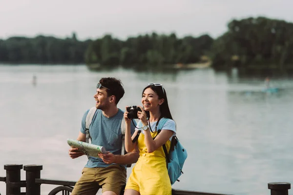 Lächelnde und asiatische Frau mit Digitalkamera und schöner Mann mit Landkarte — Stockfoto