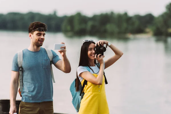 Asiático mujer tomando foto y guapo hombre usando smartphone - foto de stock