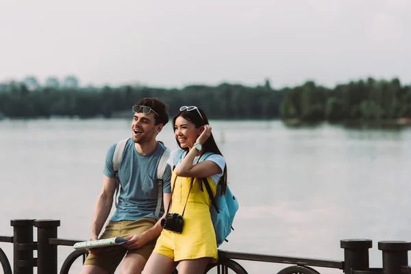Bonito homem segurando mapa e asiático mulher olhando para longe — Fotografia de Stock