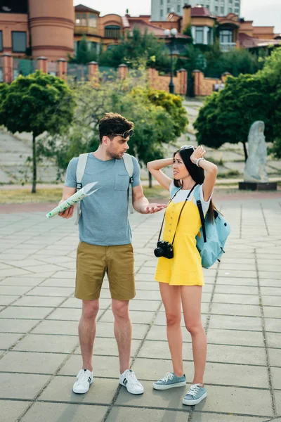 Triste y guapo hombre sosteniendo mapa y asiático mujer mirando uno al otro - foto de stock