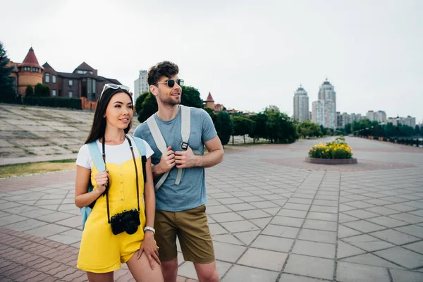 Schöner Mann und asiatische Frau mit Rucksäcken, die wegschauen — Stockfoto