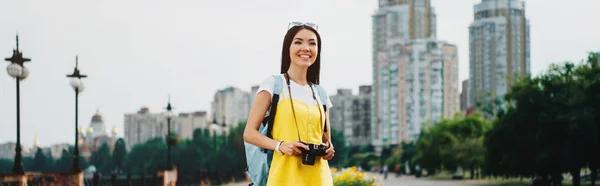 Panoramic shot of asian woman holding digital camera and looking away — Stock Photo