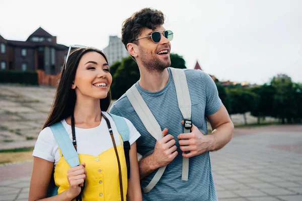 Handsome man and asian woman with backpacks looking away — Stock Photo