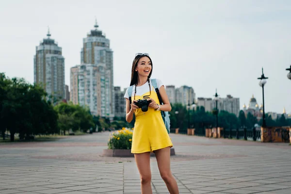 Souriant et asiatique femme tenant appareil photo numérique et regardant loin — Photo de stock