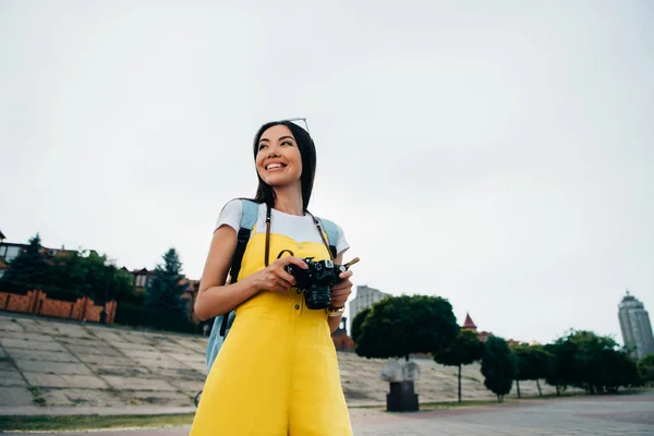 Lächelnde und asiatische Frau hält Digitalkamera in der Hand und schaut weg — Stockfoto