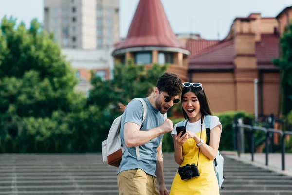 Schockierter und gutaussehender Mann und asiatische Frau schauen aufs Smartphone — Stockfoto