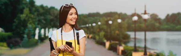 Plano panorámico de mujer asiática y atractiva sosteniendo teléfono inteligente - foto de stock
