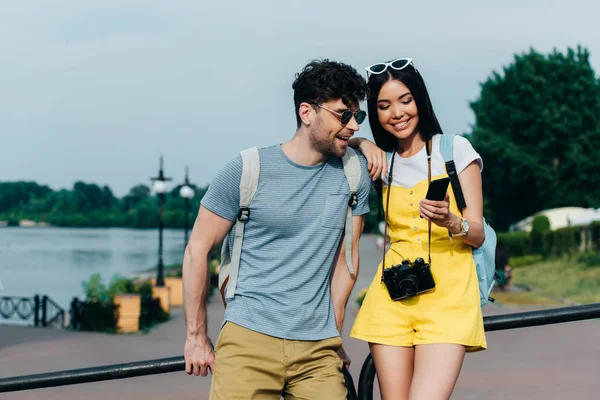 Schöner Mann und asiatische Frau lächeln und schauen aufs Smartphone — Stockfoto
