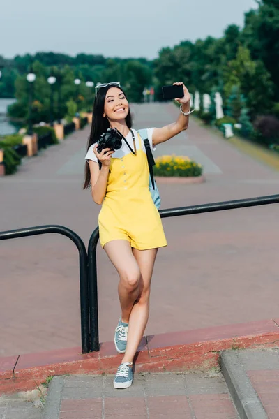 Азиатская и привлекательная женщина держит цифровую камеру и делает селфи — стоковое фото