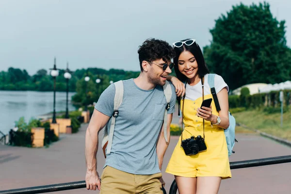 Красивий чоловік і азіатська жінка посміхаються і дивляться на смартфон — Stock Photo