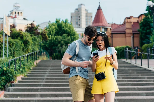 Shocked man and asian woman looking at smartphone outside — Stock Photo