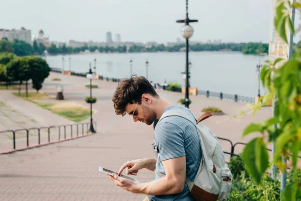 Handsome man in glasses with backpack using digital tablet — Stock Photo