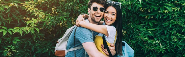 Panoramic shot of handsome man and asian woman hugging and looking at camera — Stock Photo