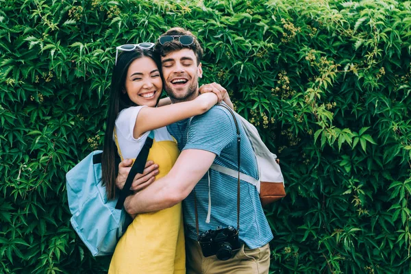 Guapo hombre y asiático mujer con cerrado ojos abrazando fuera - foto de stock