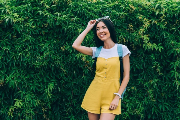 Mujer asiática y atractiva en mono amarillo sonriendo y mirando hacia otro lado - foto de stock