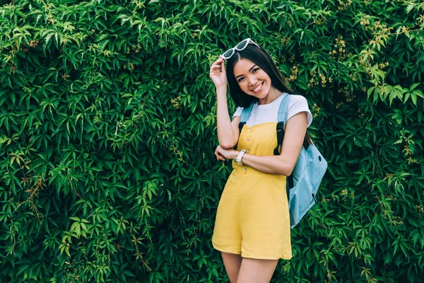 Asiático y atractivo mujer en amarillo overoles sonriendo y mirando a cámara - foto de stock