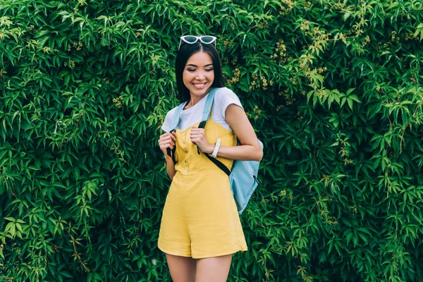 Asiática e atraente mulher em macacão sorrindo e olhando para baixo — Fotografia de Stock