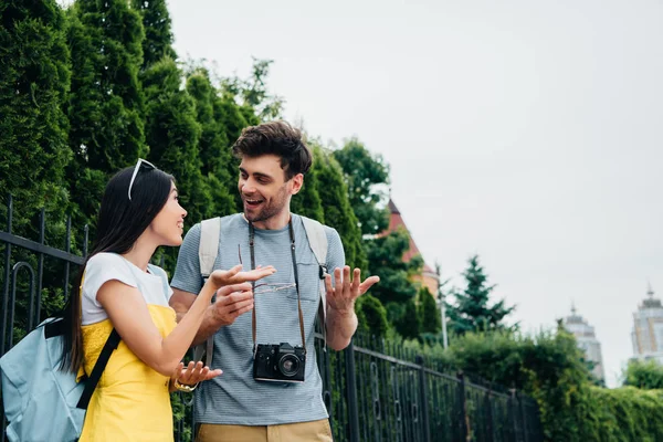 Bello uomo con digitale fotocamera parlando con sorridente asiatico donna — Foto stock