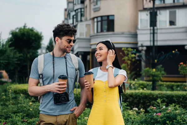 Man with digital camera and asian woman talking and holding paper cups — Stock Photo