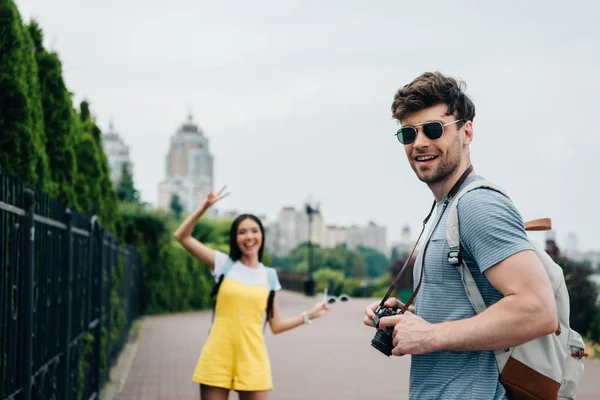 Bel homme avec appareil photo numérique et asiatique femme regardant appareil photo — Photo de stock