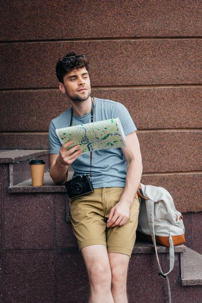 Hombre guapo en gafas sosteniendo mapa y mirando hacia otro lado - foto de stock