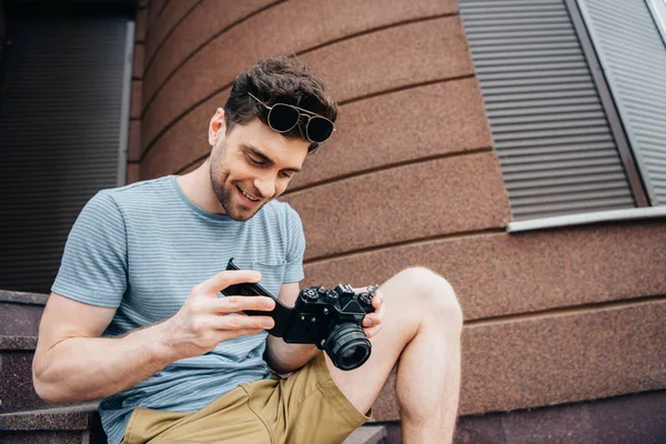Homme souriant et beau dans des lunettes regardant appareil photo numérique — Photo de stock