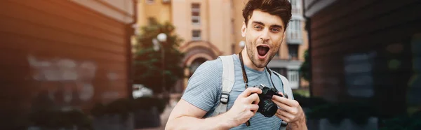 Tiro panorâmico de homem bonito em t-shirt segurando câmera digital e olhando para a câmera — Fotografia de Stock