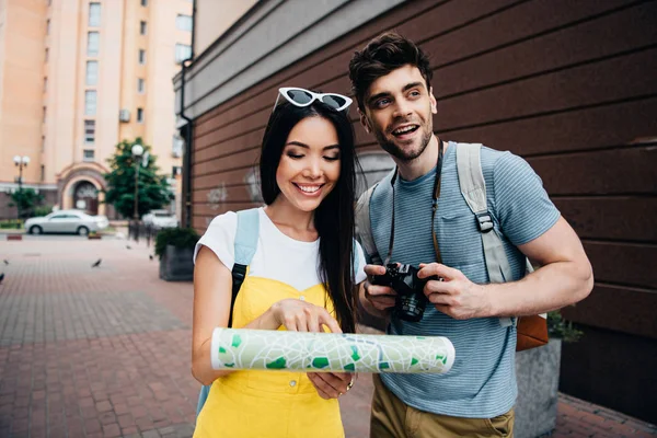 Bel homme avec appareil photo numérique regardant loin et femme asiatique tenant carte — Photo de stock