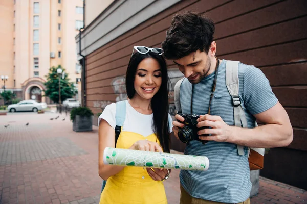Schöner Mann mit Digitalkamera und asiatische Frau beim Anblick der Landkarte — Stockfoto