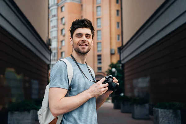 Handsome man in t-shirt holding digital camera and looking away — Stock Photo