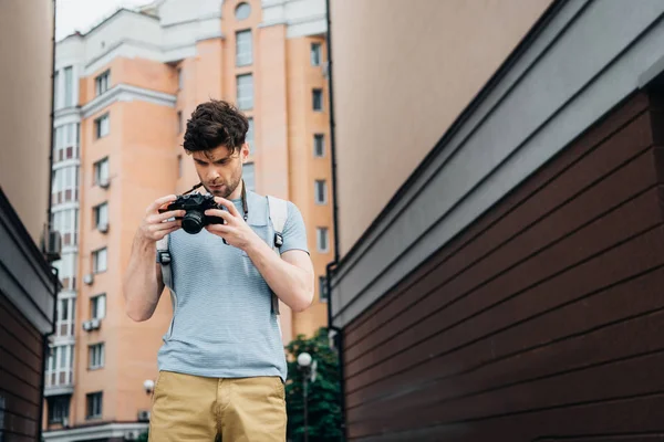 Красивый мужчина в футболке и шортах смотрит на цифровую камеру — стоковое фото
