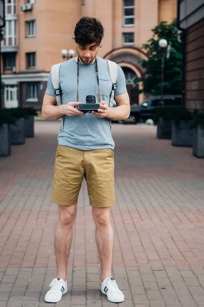 Bel homme en t-shirt et short regardant appareil photo numérique — Photo de stock