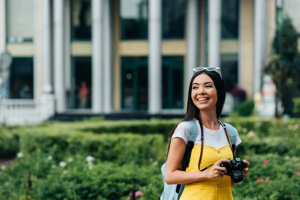 Attrayant et asiatique femme avec appareil photo numérique regardant loin — Photo de stock