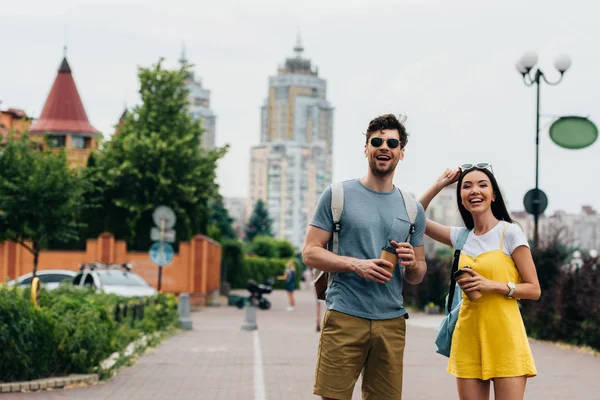 Hombre guapo y mujer asiática sonriendo y sosteniendo vasos de papel - foto de stock