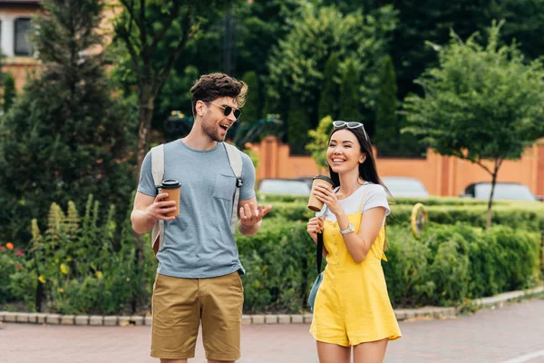 Красивый мужчина и азиатка улыбаются и держат бумажные стаканчики — стоковое фото