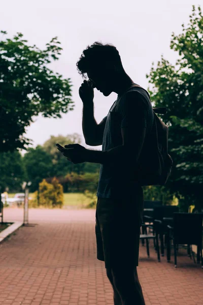 Silhouette de l'homme avec sac à dos en utilisant un appareil numérique à l'extérieur — Photo de stock