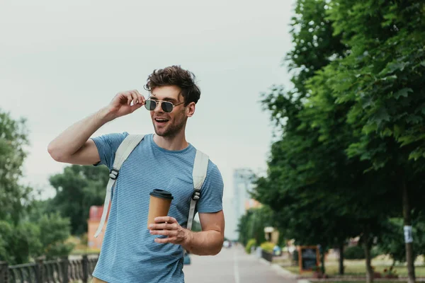 Schöner Mann im T-Shirt hält Pappbecher in der Hand und schaut weg — Stockfoto