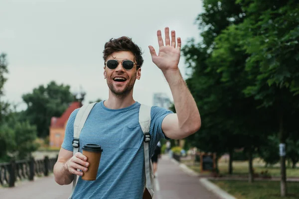 Schöner Mann im T-Shirt winkt und hält Pappbecher in der Hand — Stockfoto