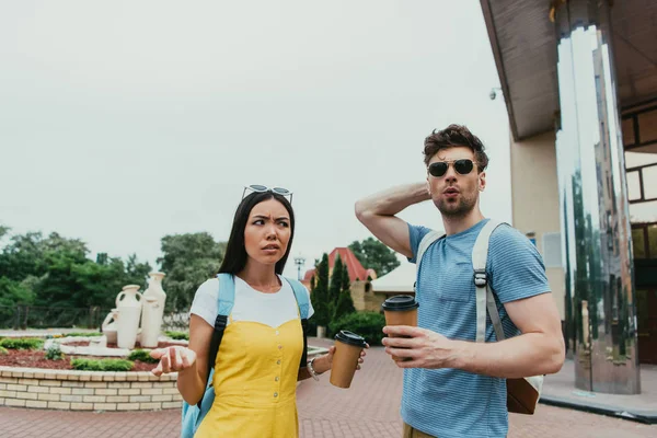 Шокированные мужчина и азиатская женщина держа бумажные чашки с кофе — стоковое фото